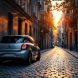 Voiture compacte garée dans une place très étroite d'une rue pavée, bâtiments proches, lumière de coucher de soleil volumétrique créant des rayons et des ombres douces, couleurs dominantes orange chaud, gris et bleu profond.