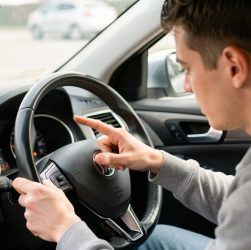 Un jeune homme révise les commandes et témoins du tableau de bord d’une voiture à l’arrêt, ambiance pédagogique et réaliste.
