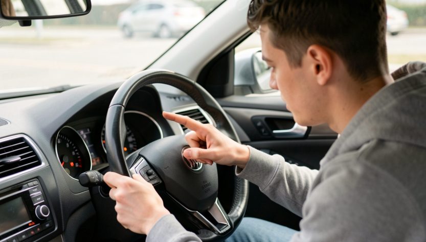Un jeune homme révise les commandes et témoins du tableau de bord d’une voiture à l’arrêt, ambiance pédagogique et réaliste.