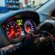 Gros plan sur le tableau de bord d’une voiture avec un voyant moteur allumé, une main en gants branche un câble de diagnostic dans un atelier automobile.