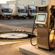 Borne de gestion de carburant sur une station privative, avec cuve et véhicules utilitaires visibles en arrière-plan.
