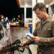 Un homme fait le plein de sa voiture dans une station-service urbaine la nuit, puis vérifie ses dépenses en consultant un terminal de paiement et des notes.