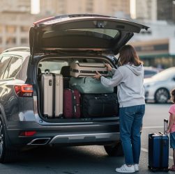 Vue arrière d’un SUV 7 places moderne, coffre ouvert, une famille charge des bagages dans le coffre sur un parking.