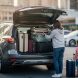 Vue arrière d’un SUV 7 places moderne, coffre ouvert, une famille charge des bagages dans le coffre sur un parking.