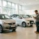 Jeune homme comparant plusieurs voitures citadines neuves dans un concessionnaire lumineux et moderne.