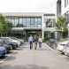 Parking d’entreprise moderne avec voitures électriques, vélos et quatre salariés se déplaçant à la lumière naturelle.
