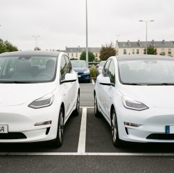 Deux voitures électriques, une compacte fabriquée en Chine et une citadine européenne, stationnées côte à côte sur un parking français avec des bornes de recharge en arrière-plan.